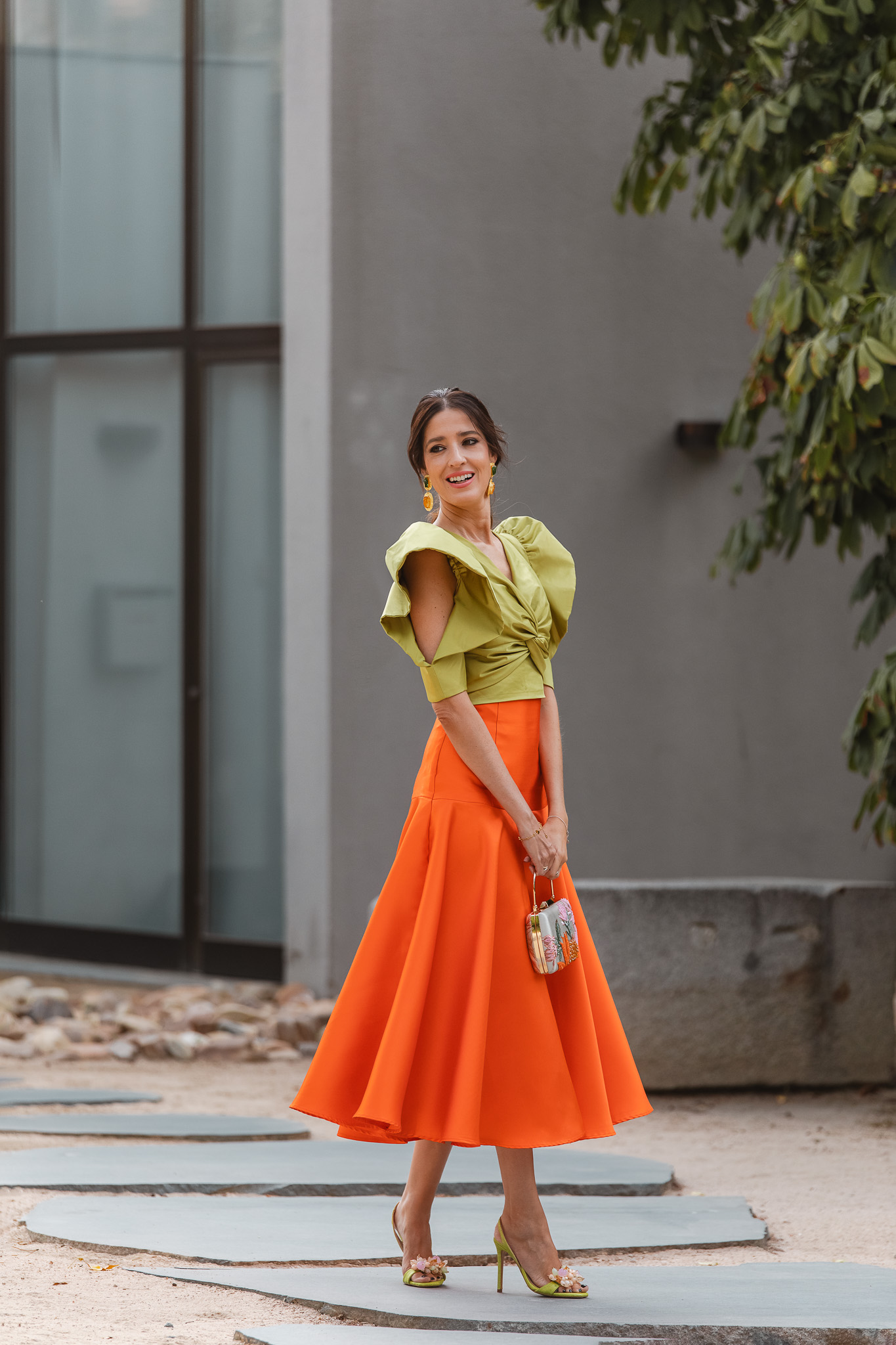 Falda naranja de vuelo y top lima con mangas abiertas, look de invitada elegante