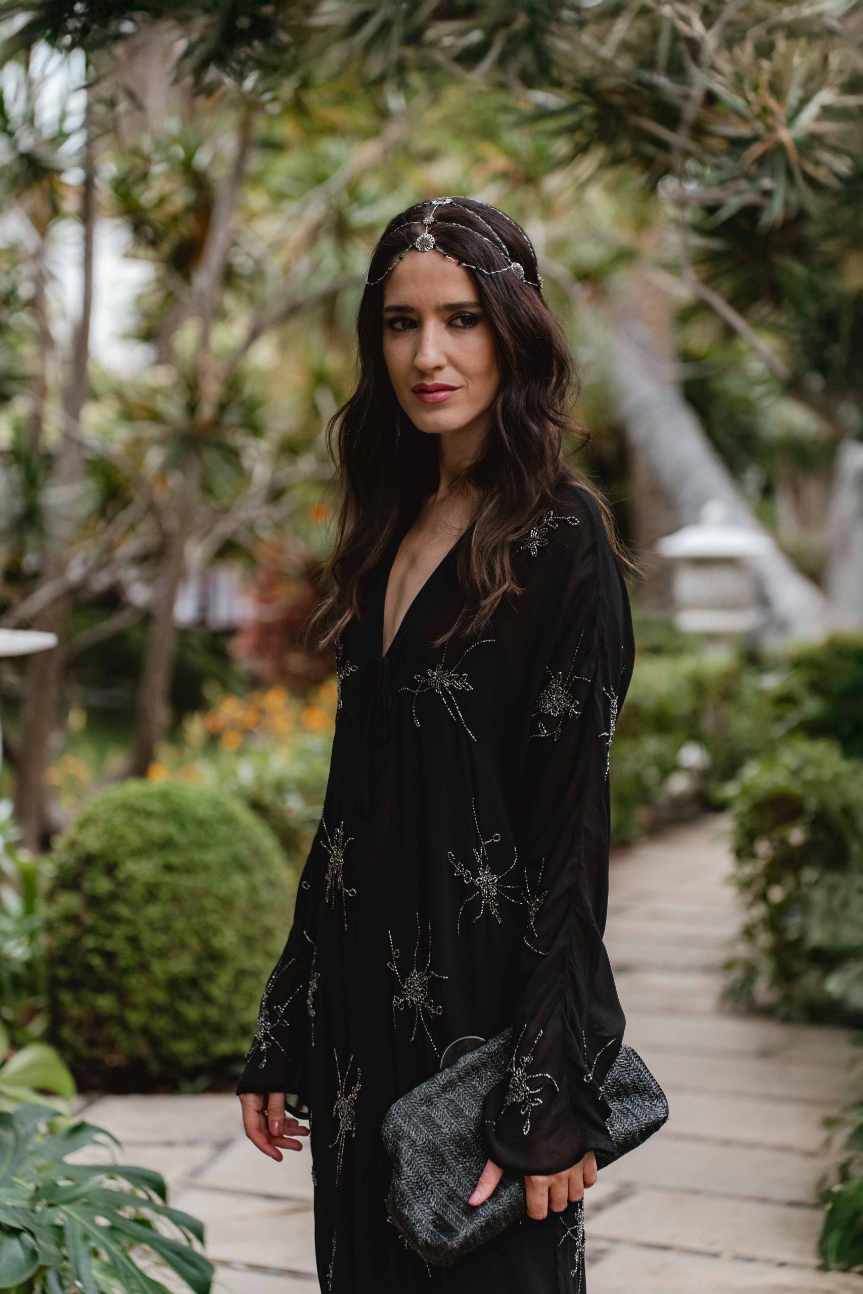 Invitada elegante con vestido negro bordado y joyas en plata, estilo boho.