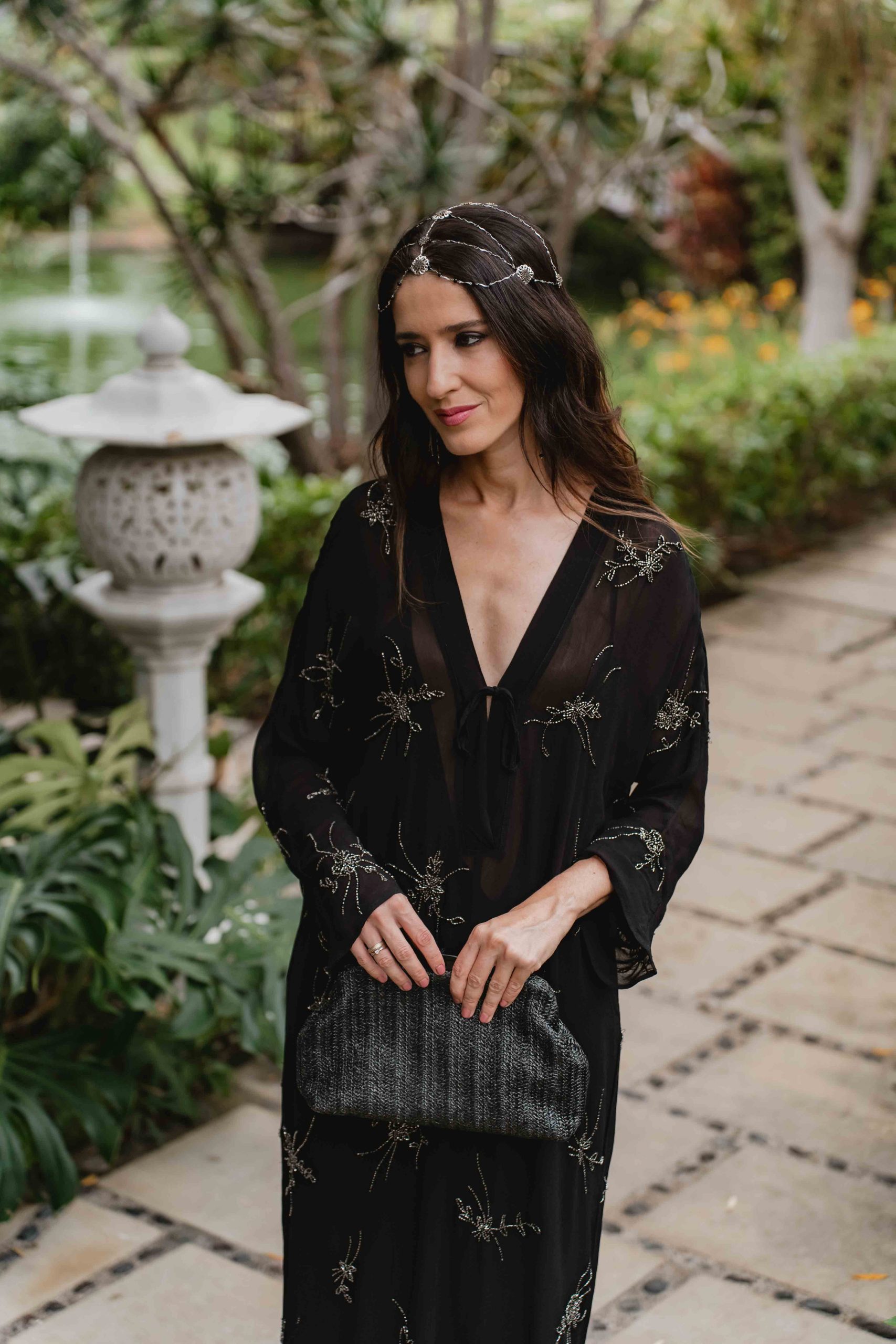 Invitada elegante con vestido negro bordado y joyas en plata, estilo boho.