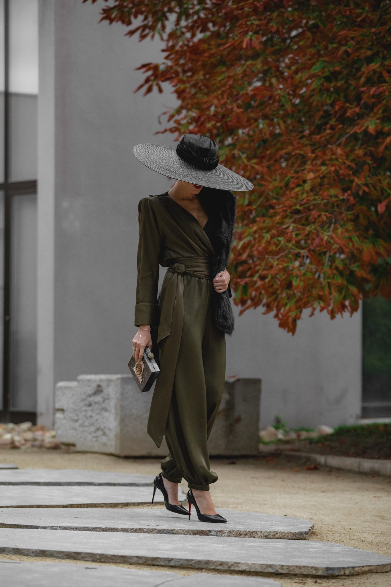 Look de invitada elegante con mono satinado verde y pamela negra.