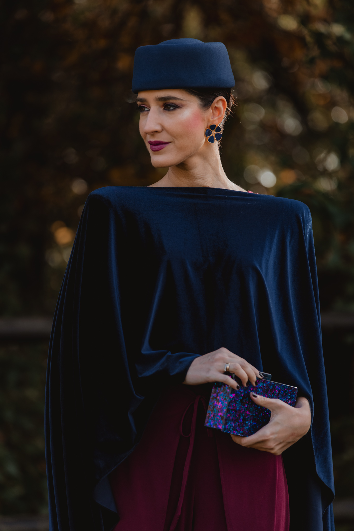 Look de invitada de invierno con jumpsuit burdeos de Magnolia Kobus y capa azul marino