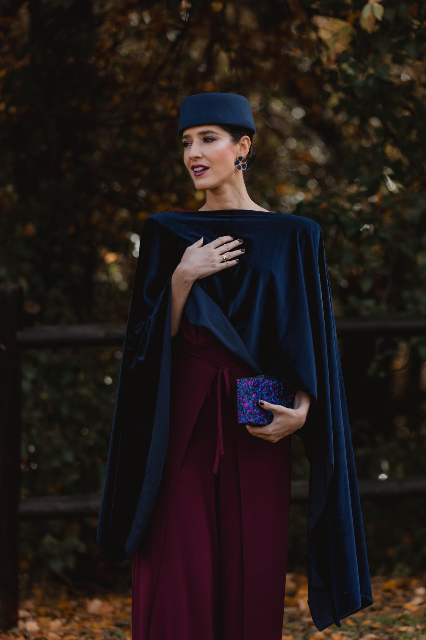 Capa de terciopelo azul marino sobre jumpsuit burdeos para boda de invierno