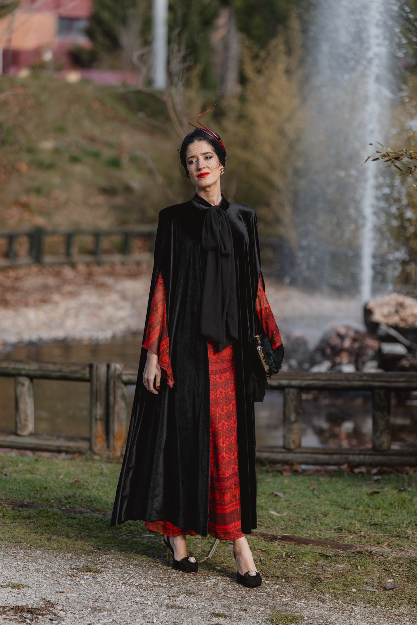 Look invitada boda invierno con vestido rojo estampado y capa negra de terciopelo