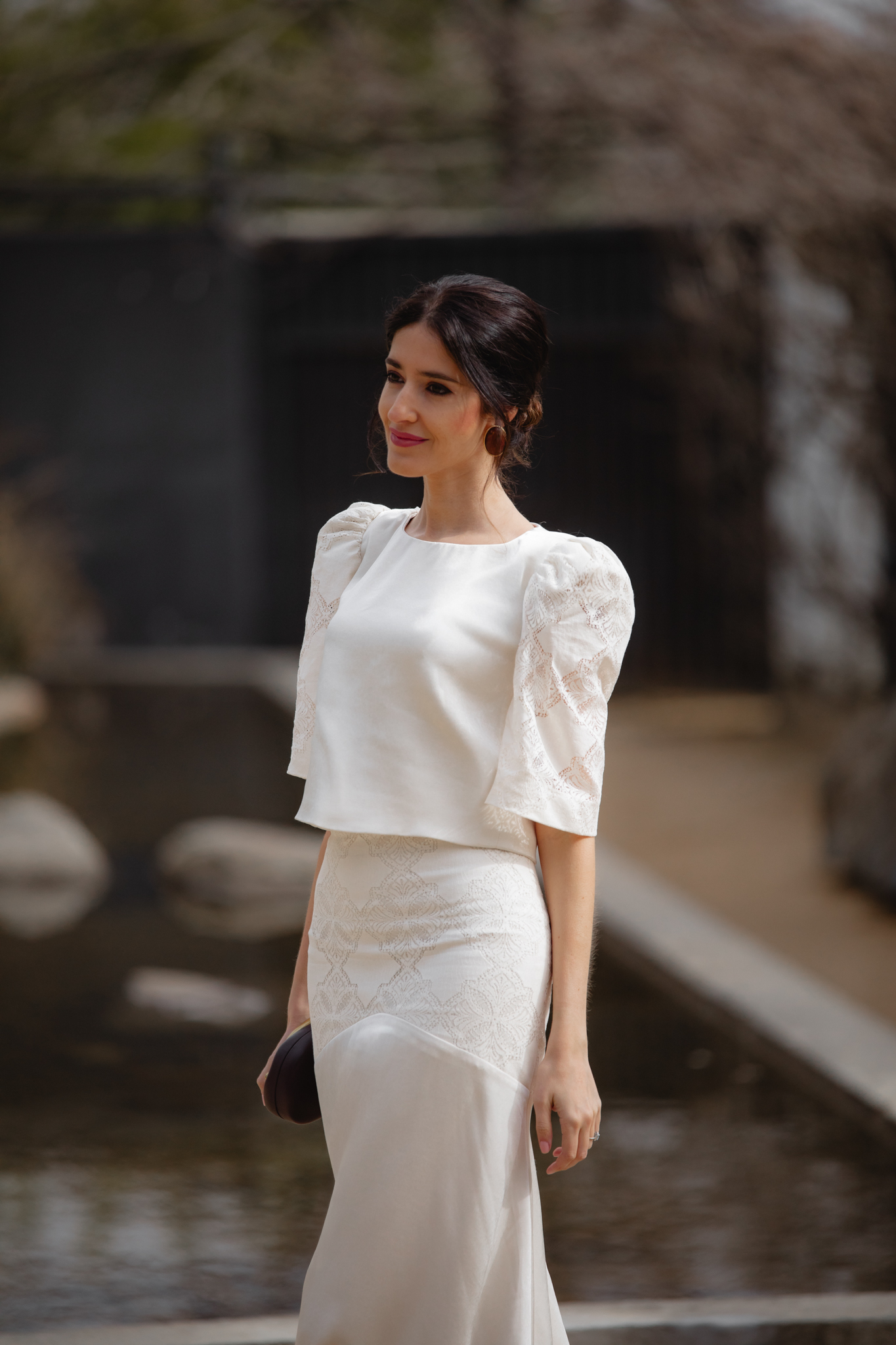 Look de comunión con blusa marfil satinada y clutch marrón chocolate.