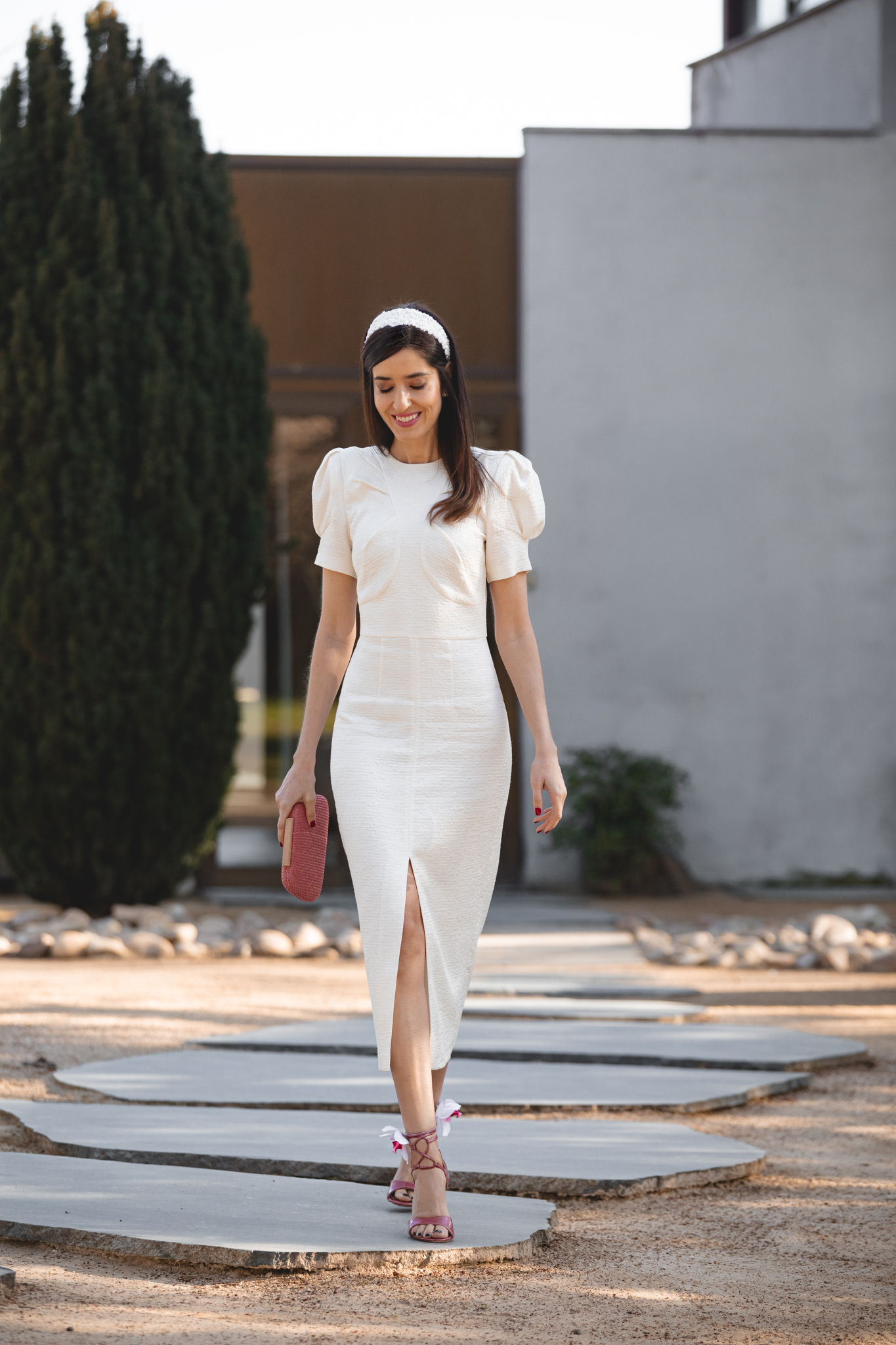 Look elegante de comunión con vestido blanco roto y bolso rosa pastel.