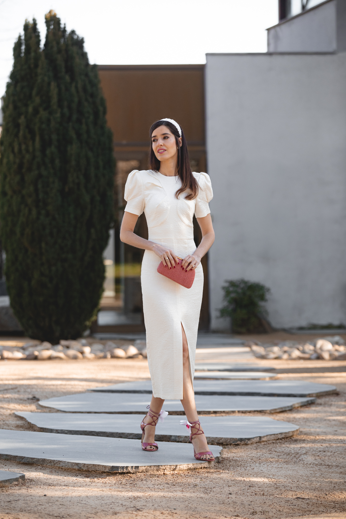 Vestido blanco roto con mangas farol y clutch rosa en look de comunión elegante.