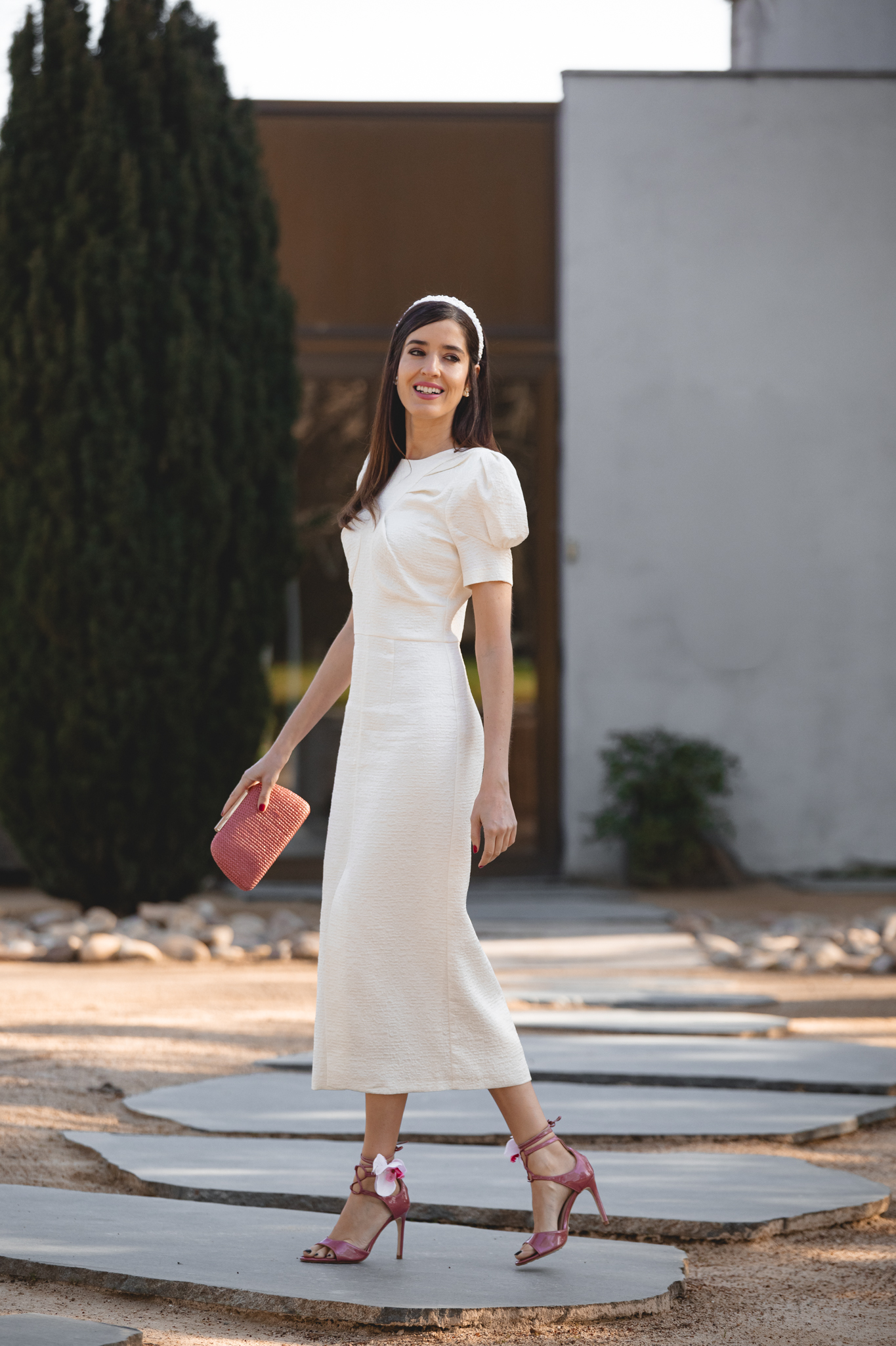 Mamá de comunión caminando con vestido blanco roto y clutch rosa.