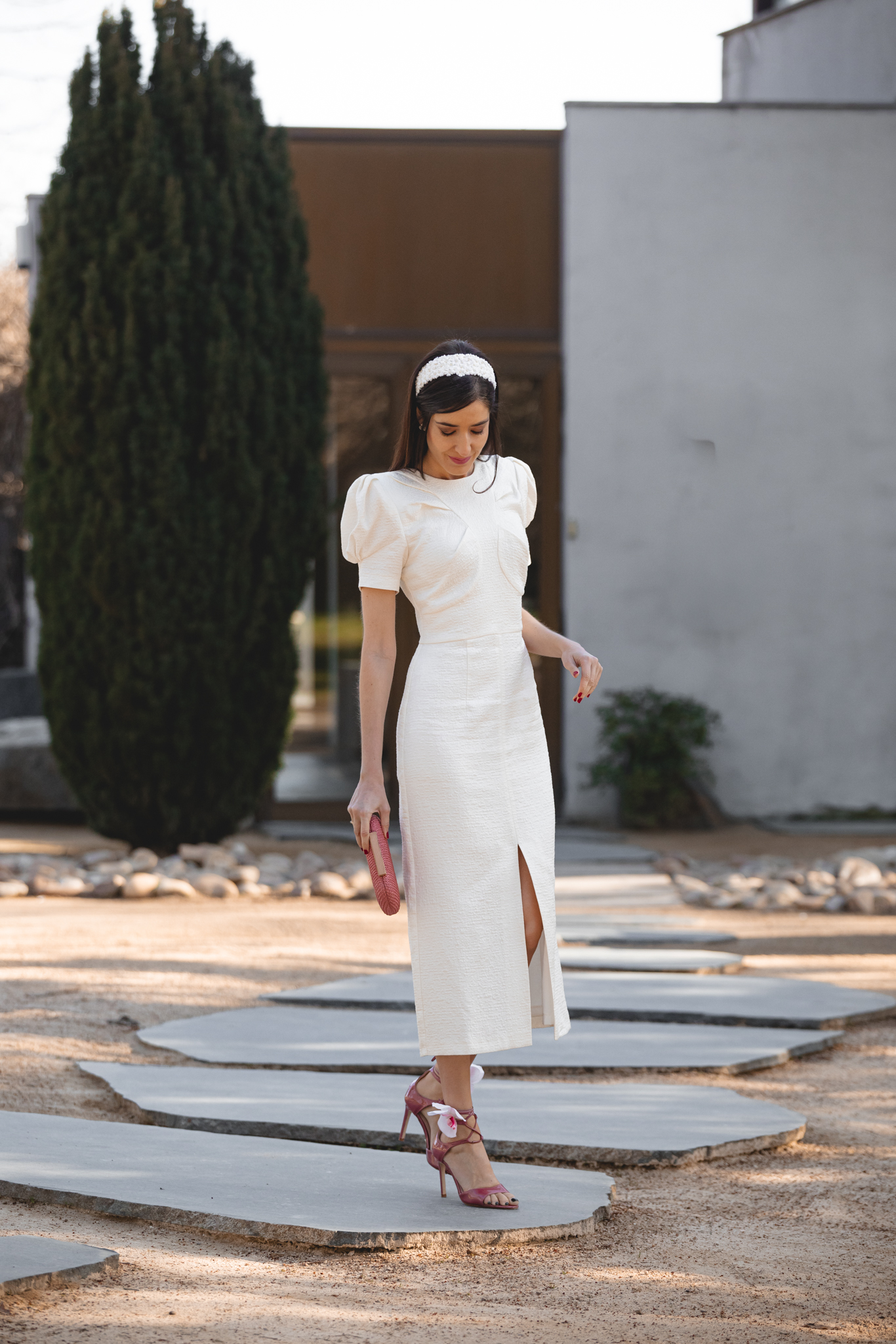 Look de comunión con vestido blanco roto y accesorios florales en tonos rosa y blanco.
