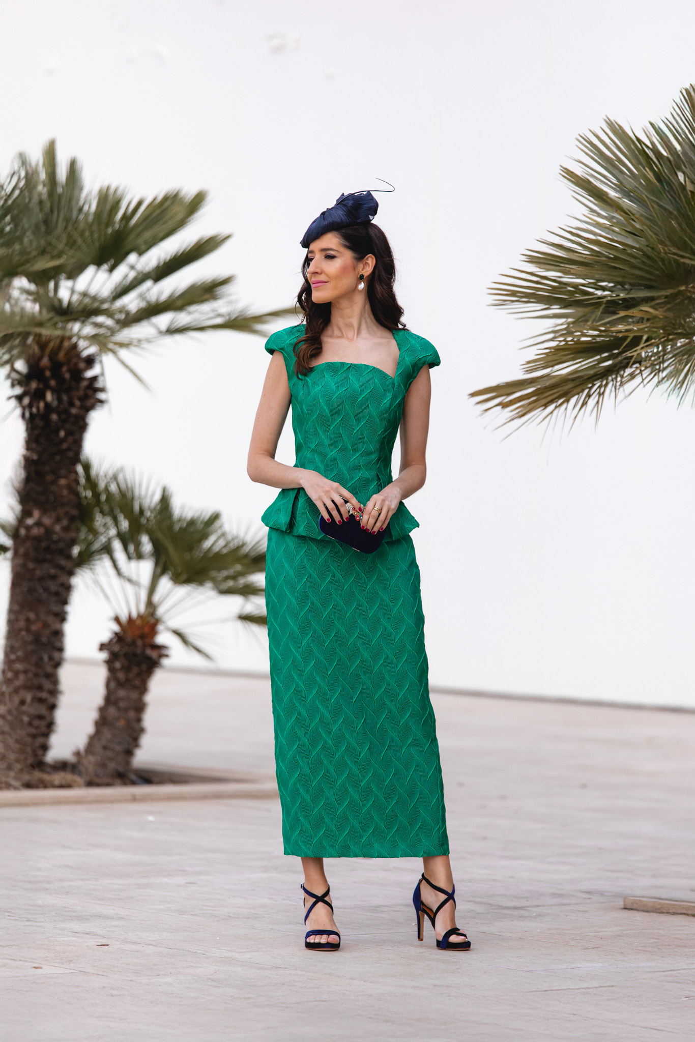 Look de invitada con conjunto verde esmeralda y tocado azul marino.