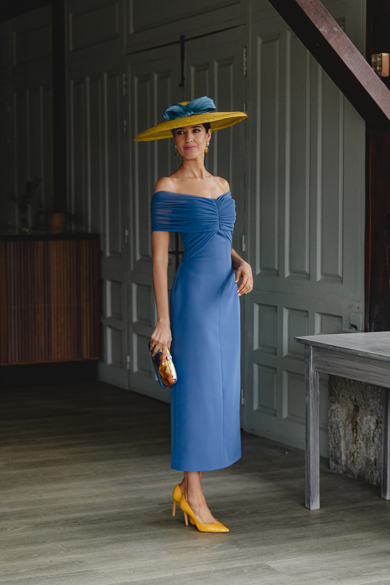 Vestido azul de invitada con escote bardot y pamela amarilla.