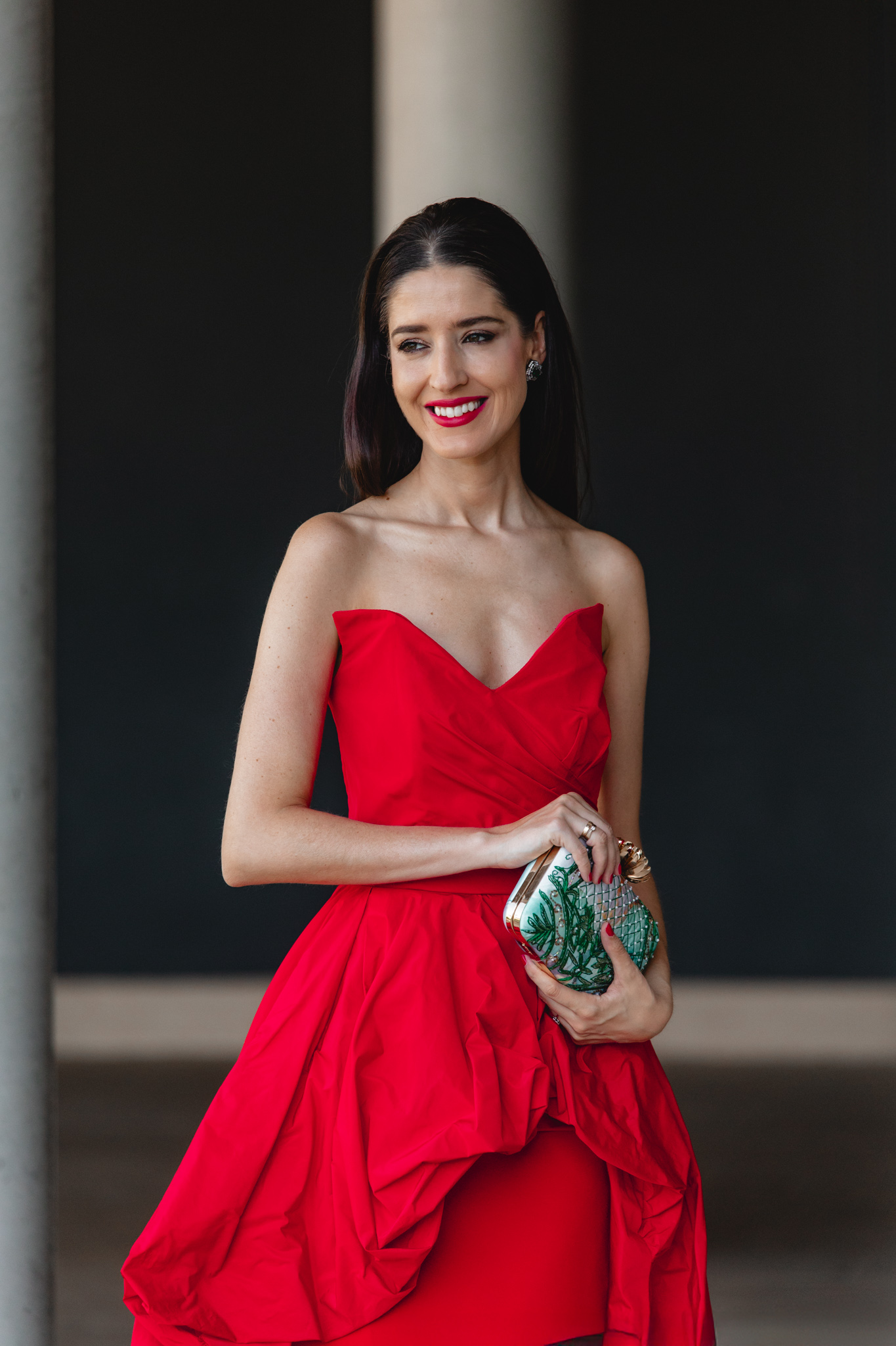 Plano medio de vestido largo rojo con escote corazón drapeado y bolso verde