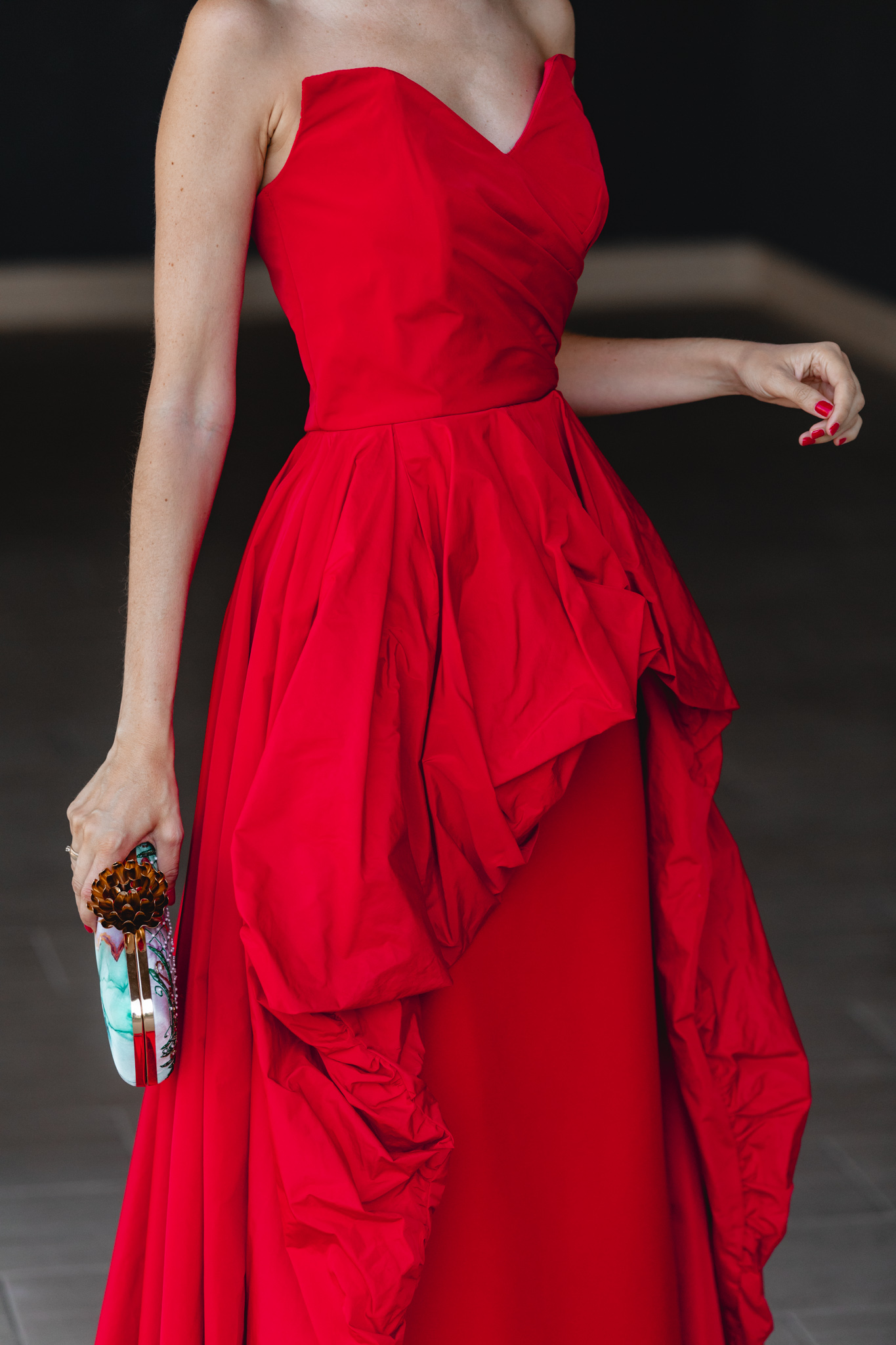 Detalle de la sobrefalda peplum del vestido largo rojo con bolso verde estampado de Acus Complementos