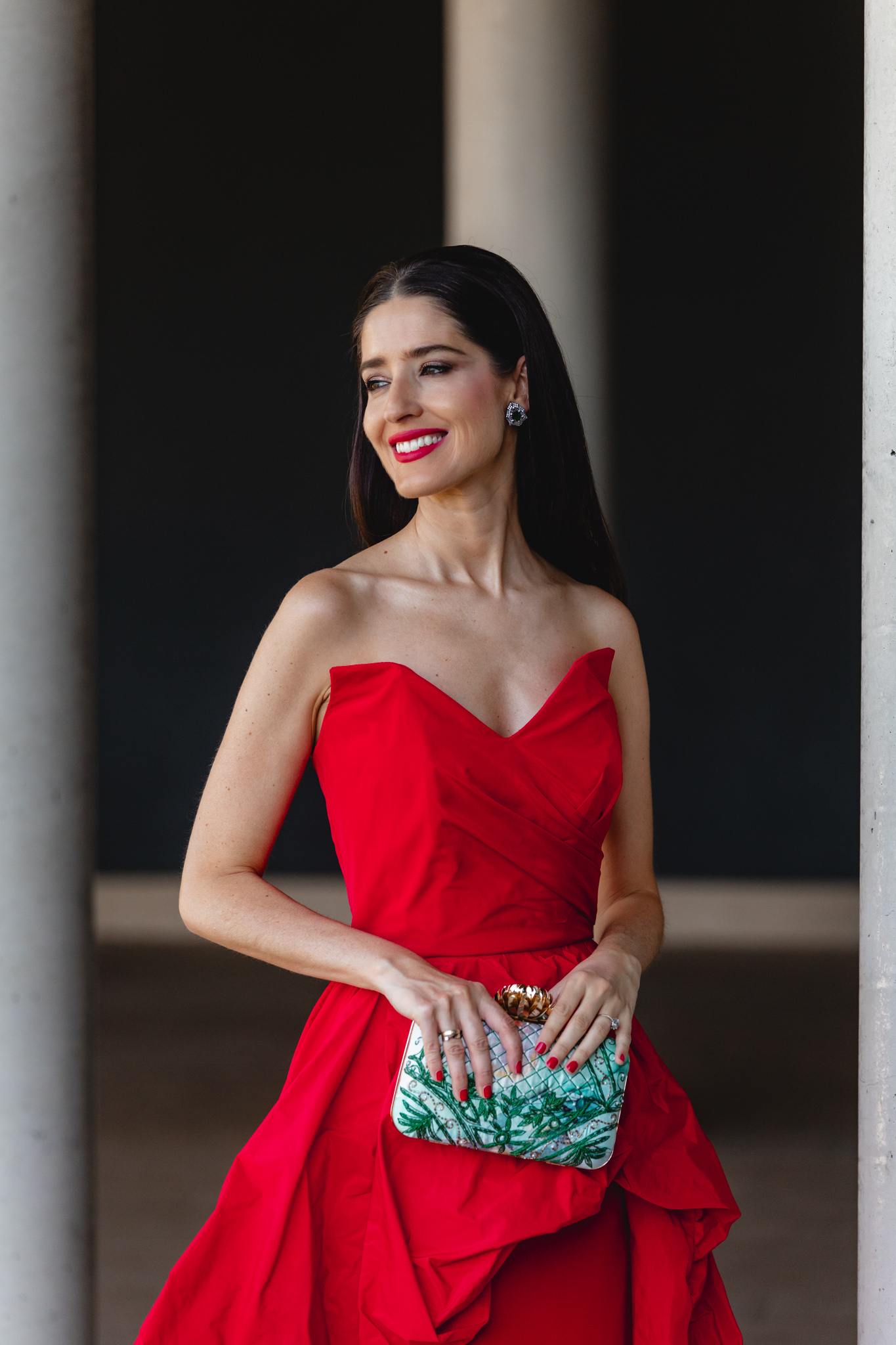 Look de invitada de primera fila con vestido largo rojo y accesorios en verde hoja