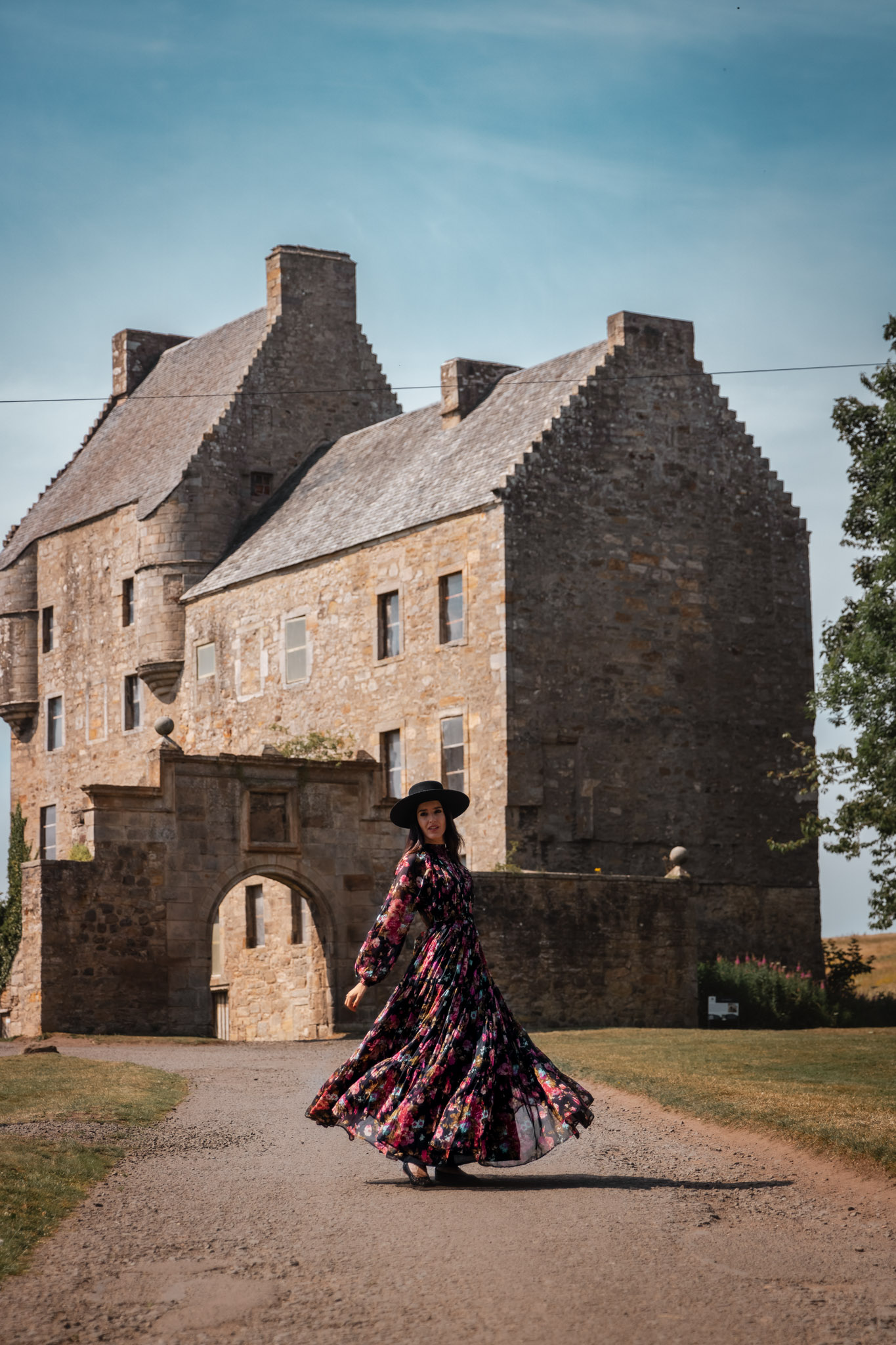 Mujer con vestido floral frente a un castillo escocés durante una excursión en coche de alquiler