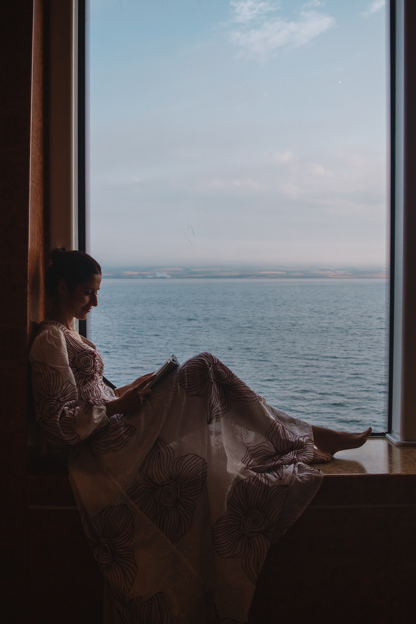 Pasajera leyendo junto a la ventana con vistas al mar en el Norwegian Star