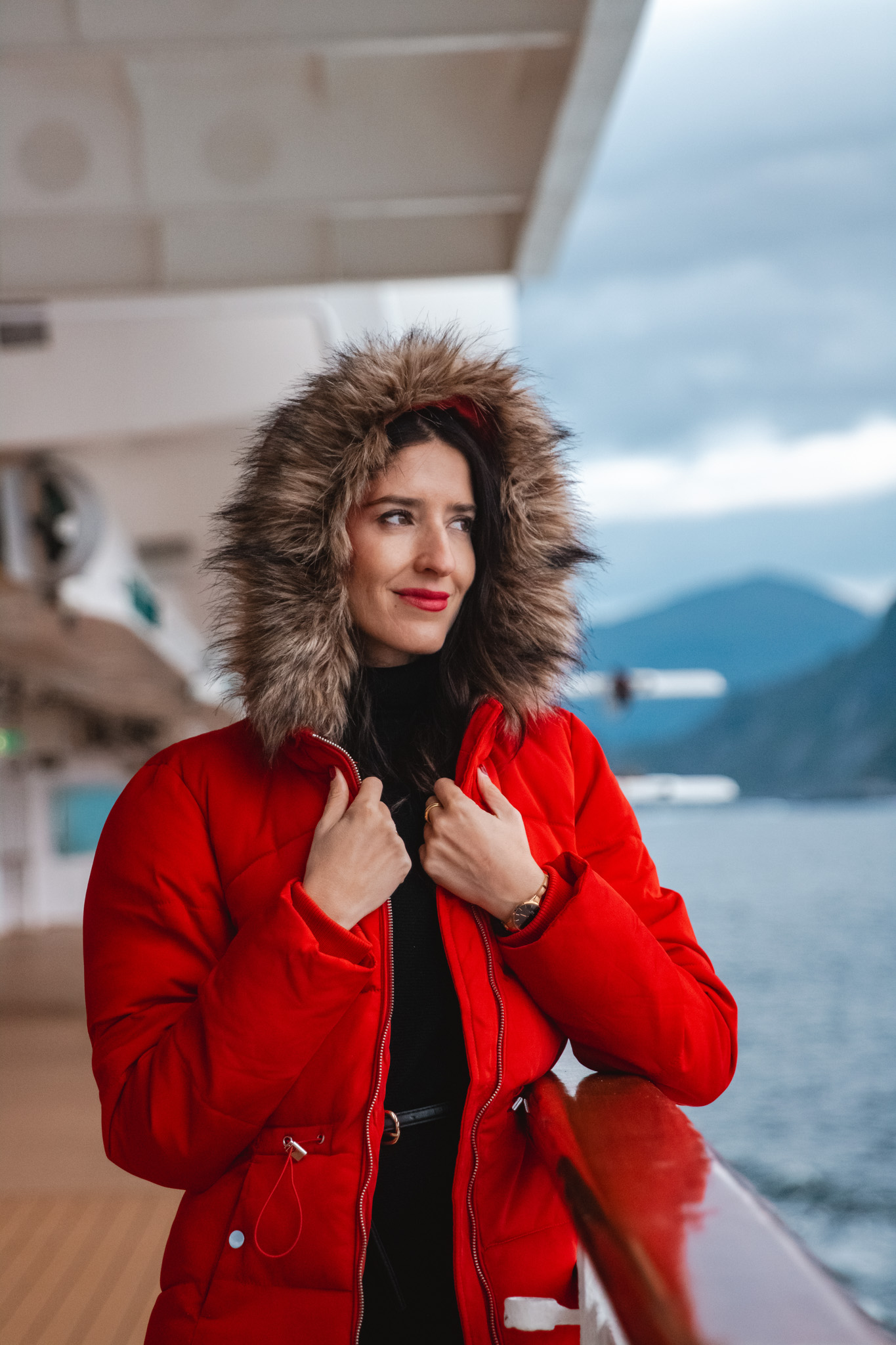 Pasajera abrigada con parka en la cubierta del crucero por los fiordos del norte de Europa