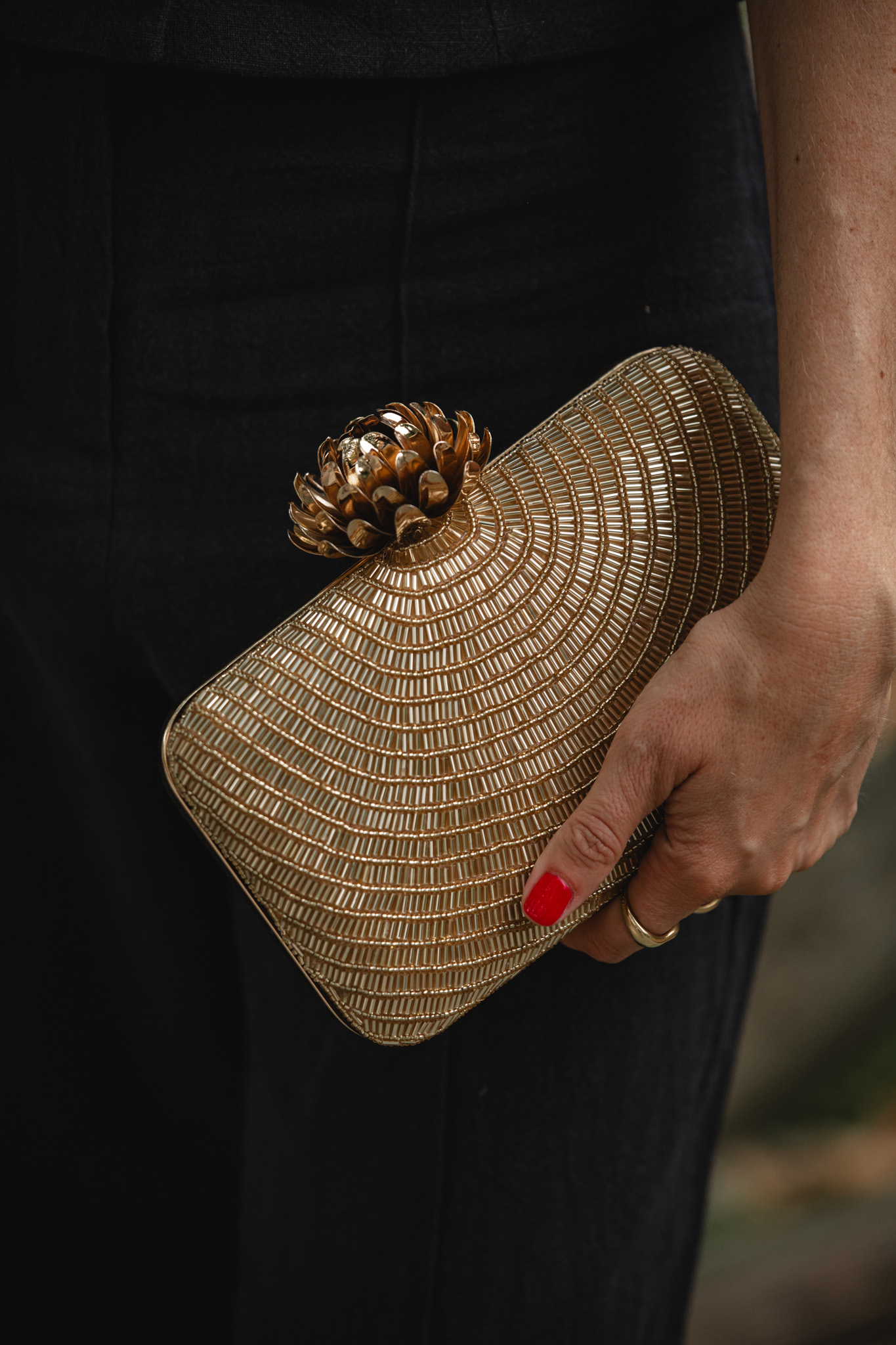 Detalle del clutch dorado trenzado con cierre en forma de piña sobre el pantalón negro